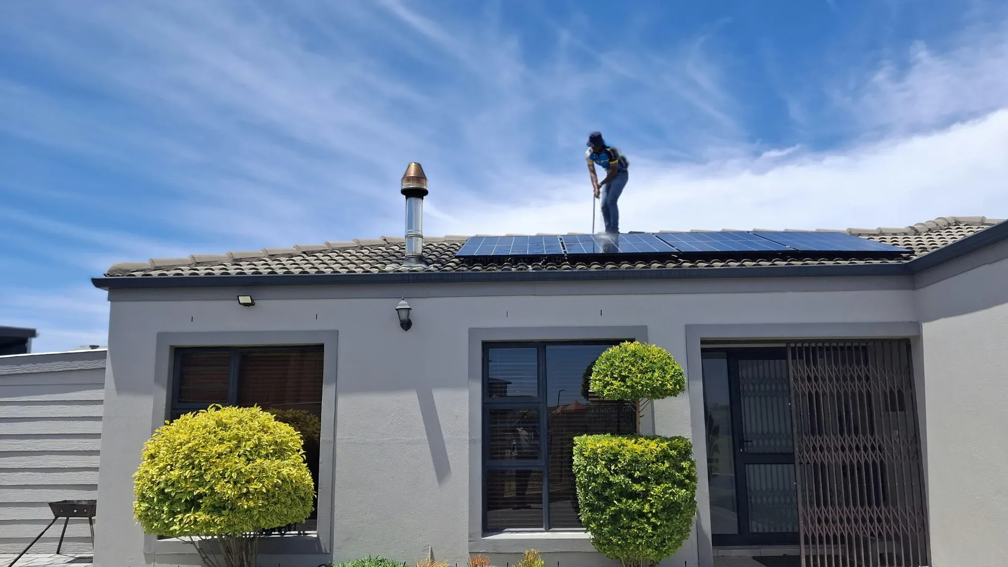 A single-story stucco home with a pitched gray tile roof and a rooftop solar panel array, photographed from the front yard on