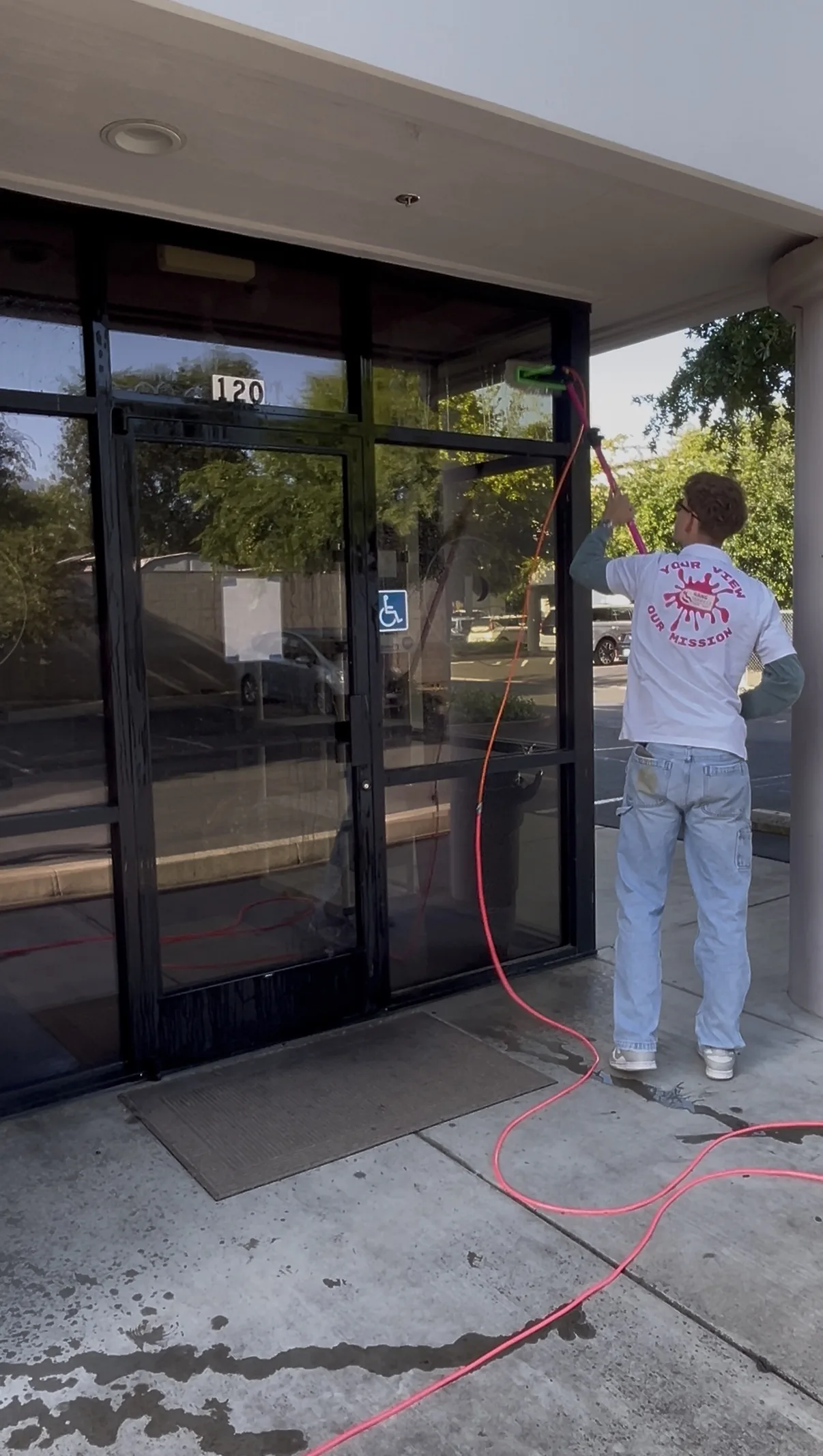 Window cleaner using squeegee to clean storefront glass doors at commercial building entrance.